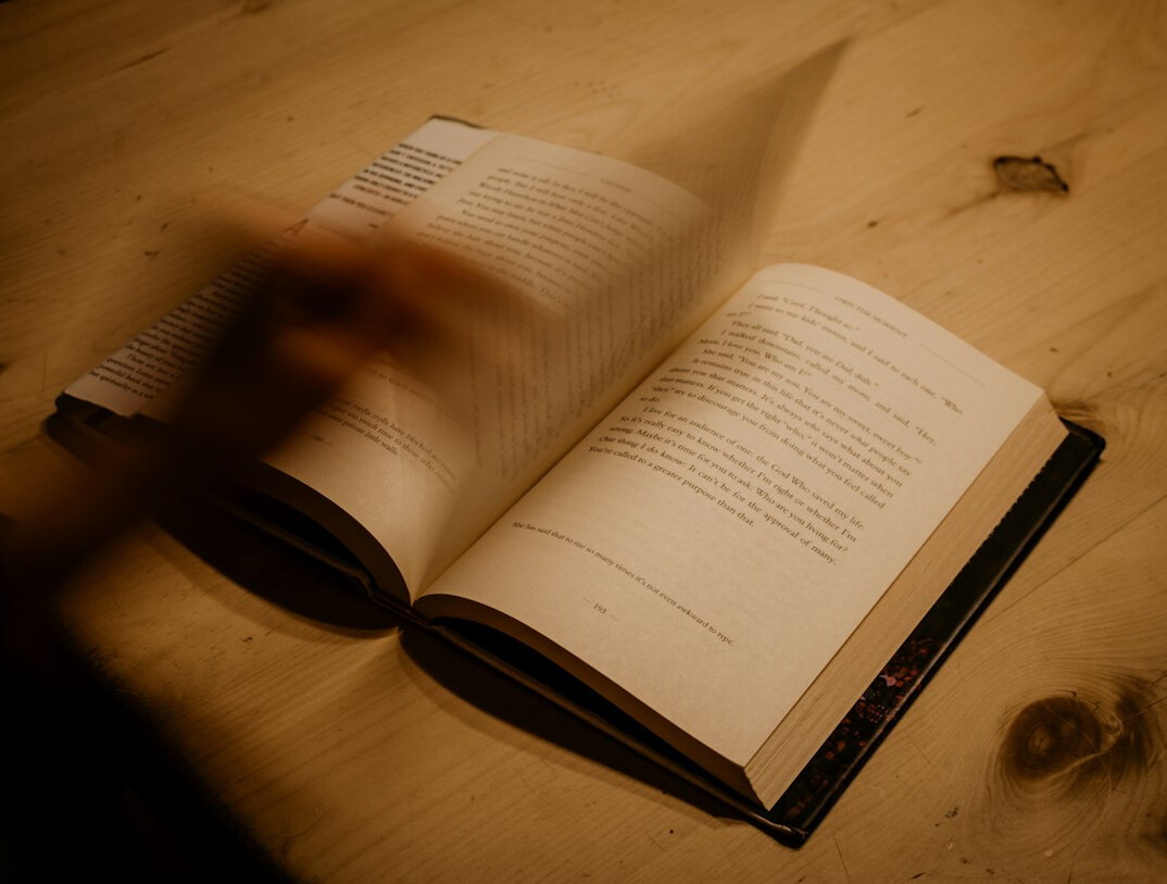 Open mystery novel on a table under dim warm lighting