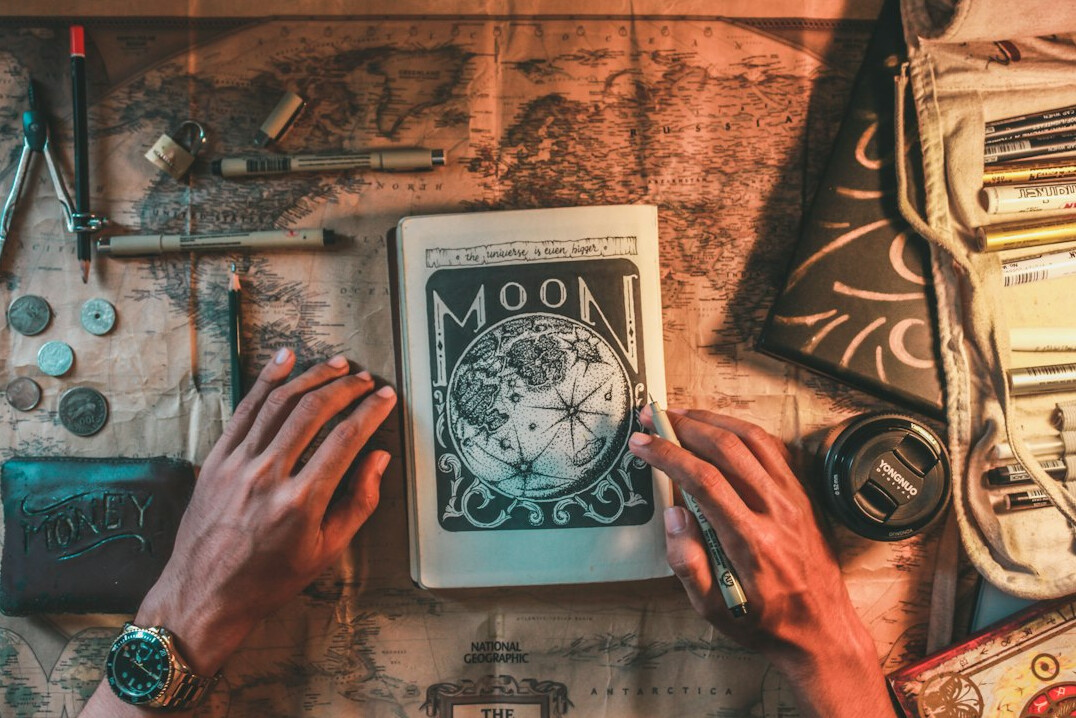 Hands writing in a notebook beside an old map and compass